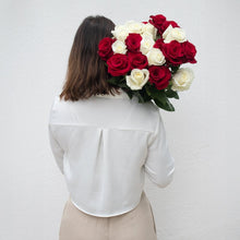 Person holding a bouquet of red and white roses against a plain background