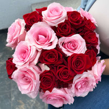 Bouquet of red and pink roses held by a person on a gray floor.
