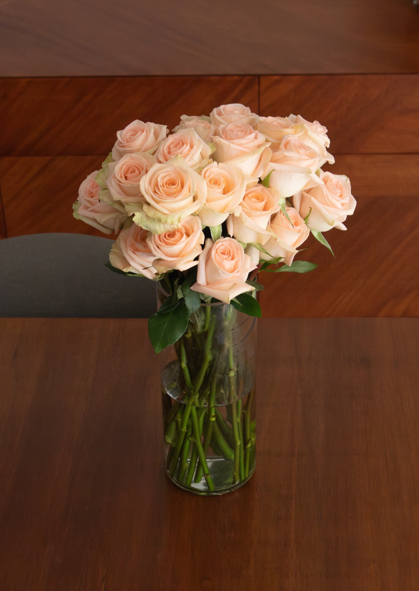 Peach roses in a clear vase on a walnut dining table